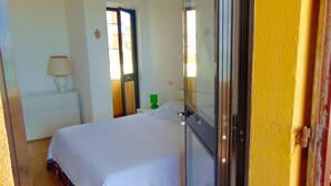 Un dormitorio con una cama, una mesita de noche, una lámpara, una botella verde y una puerta.