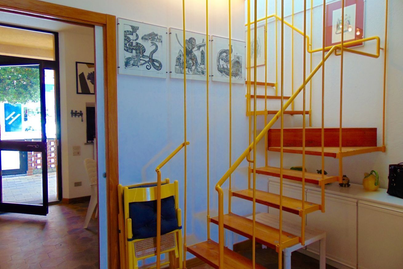 Eine Treppe mit gelben Geländern, ein Sessel mit blauer Sitzkissen und Kunstwerke an der Wand.