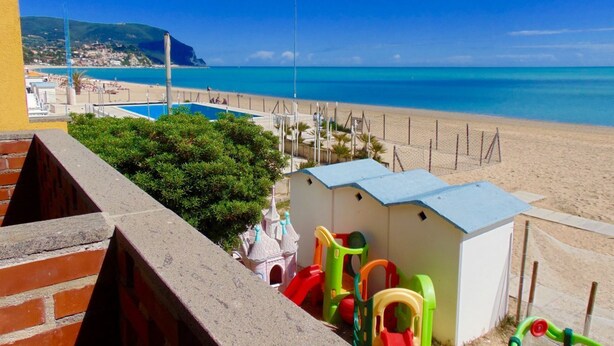 Vista de una playa con piscina, zona de juegos y un pequeño edificio.