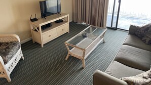 Ein Hotelzimmer mit einem Fernseher auf einem Holztisch, einem Glastisch, einer Couch und einem Korbsessel.