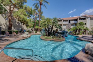 A swimming pool with a waterfall feature, surrounded by lounge chairs and palm trees. - Las Vegas Condo minutes from the Strip, Team Mobile and Allegiant Stadium (Las Vegas)