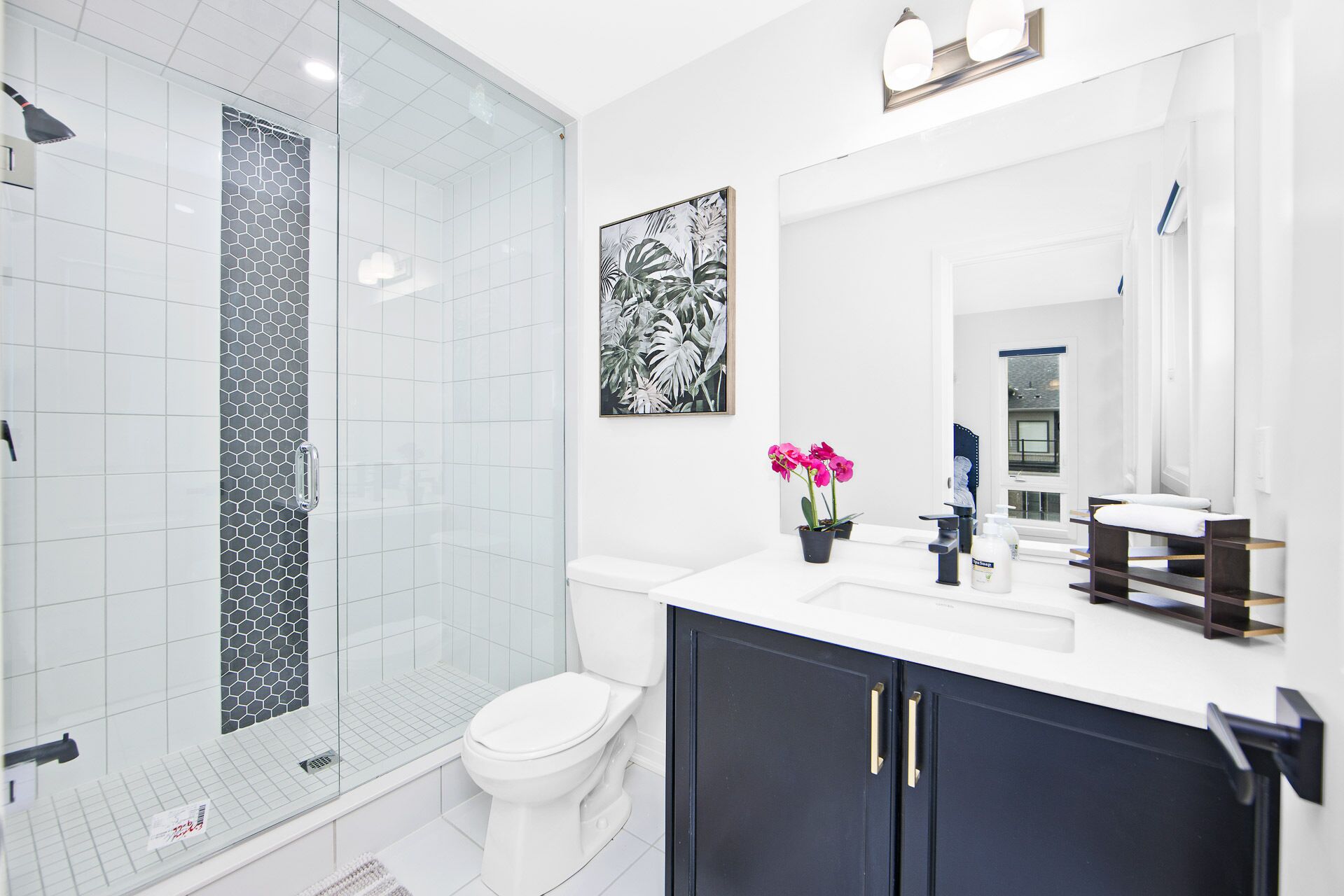 A modern bathroom with a glass shower enclosure, a white toilet, a dark vanity with a mirror, and a potted orchid.