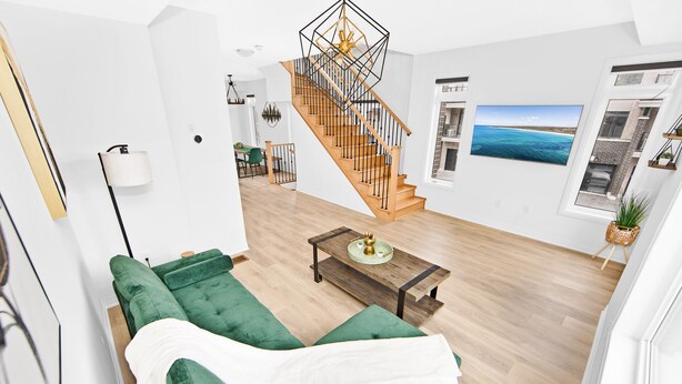 Un salon moderne avec un canapé vert, une table basse en bois et un escalier doté d’une rampe aux motifs géométriques.
