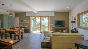 A modern living room with a sofa, a dining table with chairs, a TV, and a large window. - Cozy home in Marsaglia with kitchen (Marsaglia)