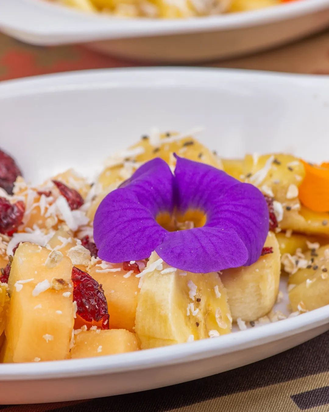 A bowl of fruit salad with a purple flower garnish.