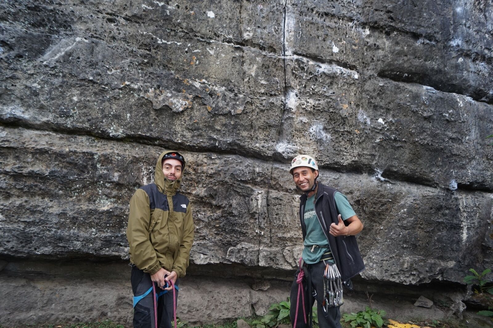 Zwei Personen stehen vor einer felsigen Klippe mit Kletterausrüstung.