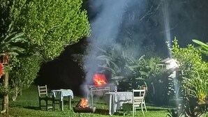 Escena nocturna al aire libre con fuego, sillas y una mesa.