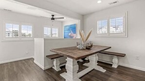 A dining area with a wooden table and benches, white walls, and large windows. - Seaside Breeze - 4BR 3BA 5 min. Walk to Beach (Kill Devil Hills)
