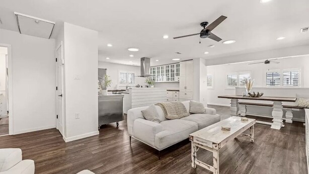 A spacious living area with a sofa, coffee table, and a dining table. There is a kitchen in the background with white cabinets and a window. - Seaside Breeze - 4BR 3BA 5 min. Walk to Beach (Kill Devil Hills)