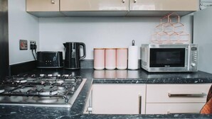 Cozinha com fogão a gás, cafeteira, micro-ondas e um conjunto de chávenas cor-de-rosa.