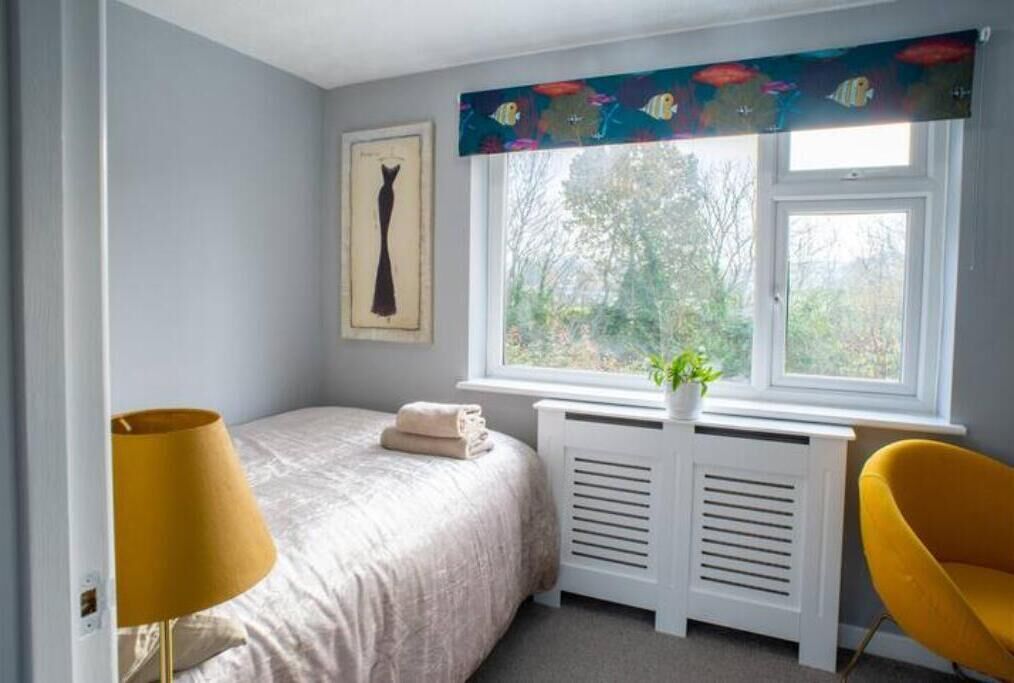 A bedroom with a bed, a radiator, a window with a view of greenery, and a yellow chair.