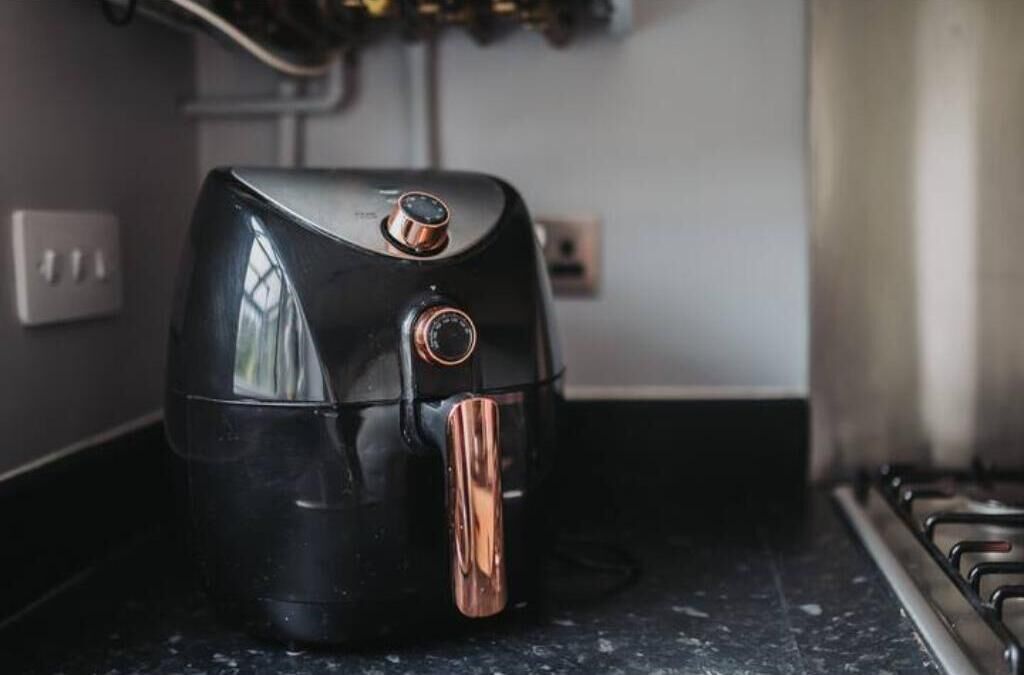 A black air fryer on a kitchen counter with a stainless steel range hood above.
