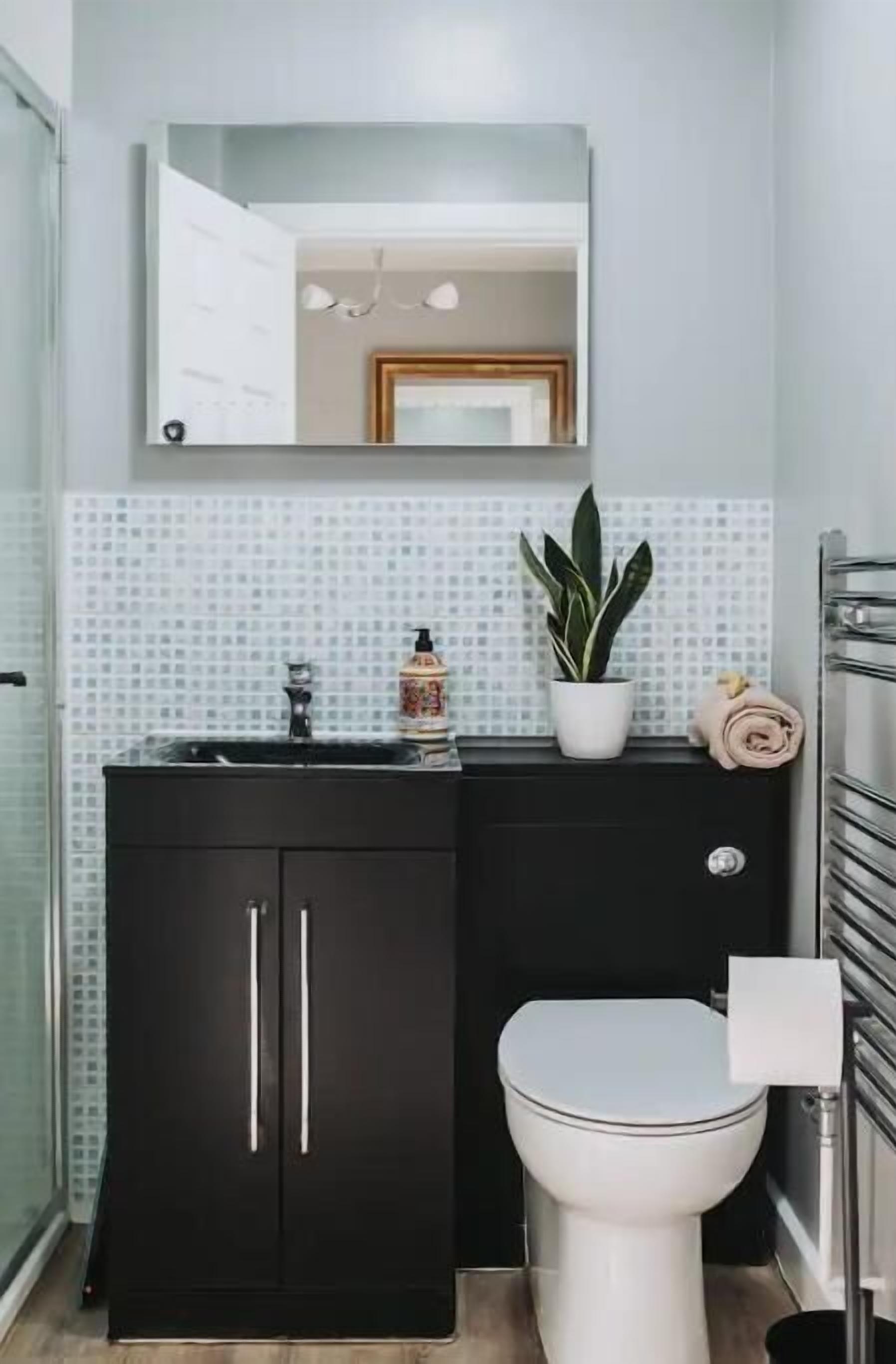 A bathroom with a black cabinet, a white toilet, a mirror, a sink, a potted plant, and a towel.