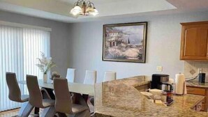 A modern kitchen with a granite countertop, a dining area with a table and chairs, and a hanging light fixture. - Hello guests, welcome to our ranch house in a quiet neighborhood. (Urbandale)