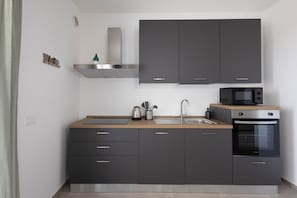 Une cuisine moderne avec des meubles de couleur sombre, une hotte de cuisinière en acier inoxydable, un four à micro-ondes et un four traditionnel.