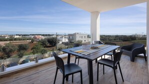 Un balcón con mesa y sillas, con vistas a una zona costera con edificios y vegetación.
