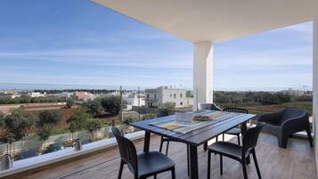 Ein Balkon mit Tisch und Stühlen, der auf eine Küstenlandschaft mit Gebäuden und Grünflächen blickt.