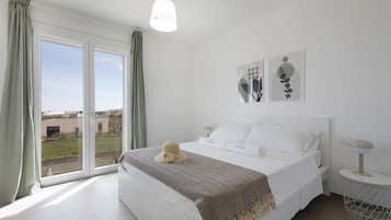 Ein Schlafzimmer mit einem großen Bett, Blick durch eine Schiebetür, einer Hängeleuchte und zwei an der Wand befestigten Kunstwerken.