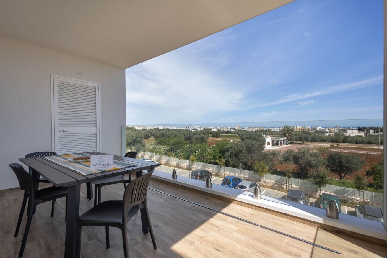 Un balcón con mesa y sillas, vista panorámica de la ciudad, y un cartel que dice 'WePuglia'.