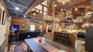 L’intérieur d’un chalet rustique comprend un coin repas en bois, des tabourets de bar, un canapé et une cuisine équipée d’une cuisinière et d’un réfrigérateur.
