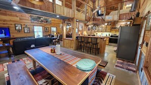 L’intérieur d’un chalet rustique comprend une table à manger en bois, des tabourets de bar, un canapé et un coin cuisine.
