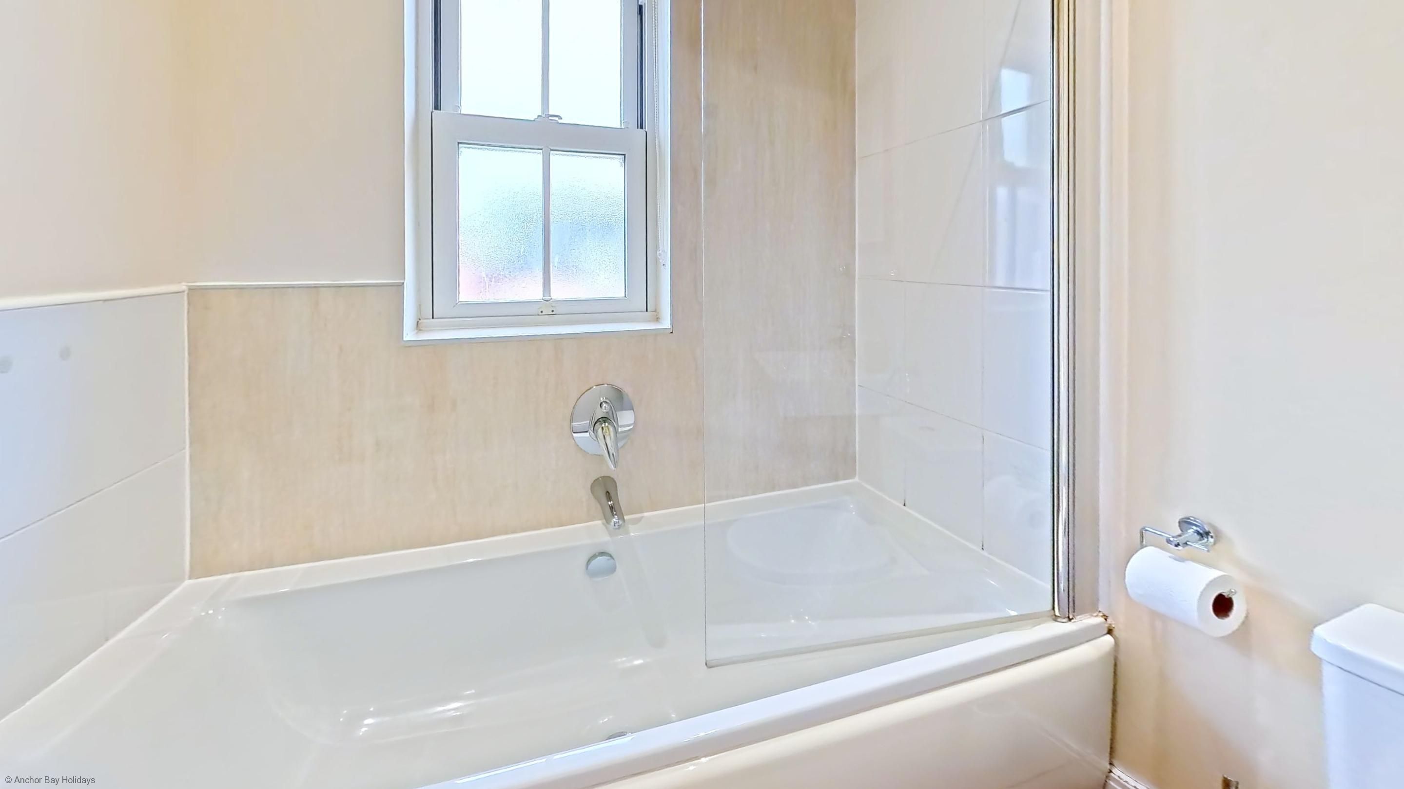 Un baño con bañera, ventana y retrete.