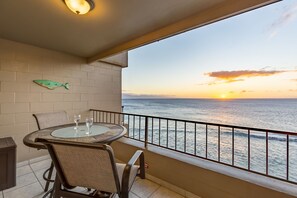 Ein Balkon mit Tisch und Stühlen, eine Fischdekoration an der Wand und Blick auf den Ozean bei Sonnenuntergang.
