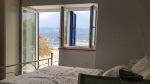 Um quarto com uma cama, uma mesa com uma tigela de frutas, um copo e um vaso.