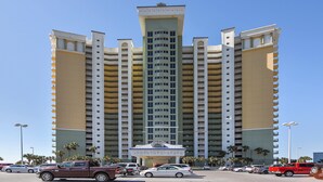 A multi-story hotel with a central atrium, multiple balconies, and a parking lot with several cars.
