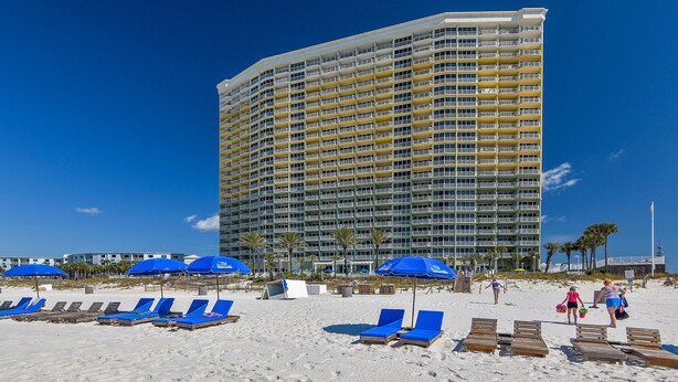 A beachfront hotel with multiple balconies, sun loungers, and blue umbrellas.