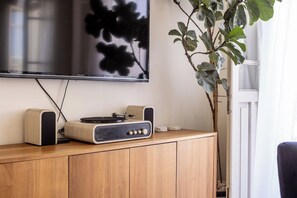 A flat-screen TV mounted on a wall, a wooden cabinet with a turntable and speakers, and a potted plant.