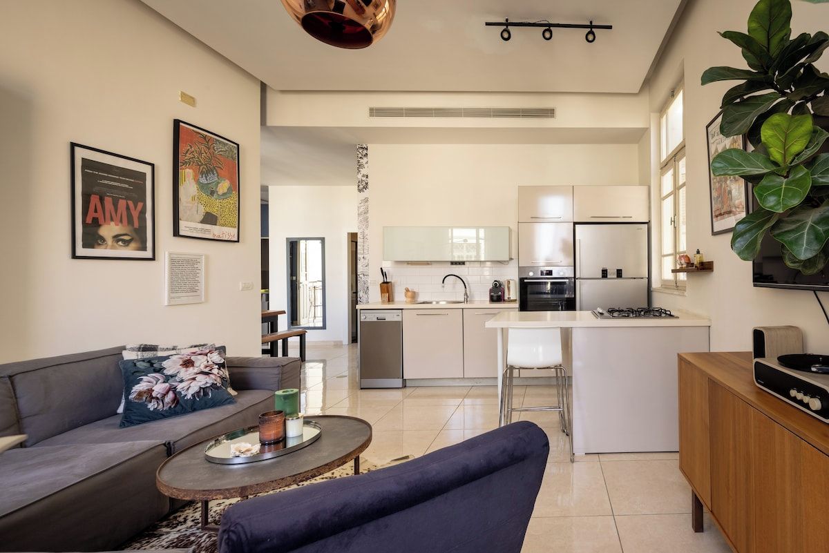 A modern living room with a sofa, a coffee table, and a kitchen in the background.