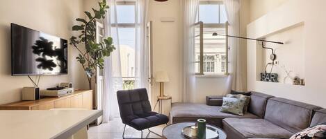 A modern living room with a flat-screen TV, a sofa, a dining table, and a coffee table.