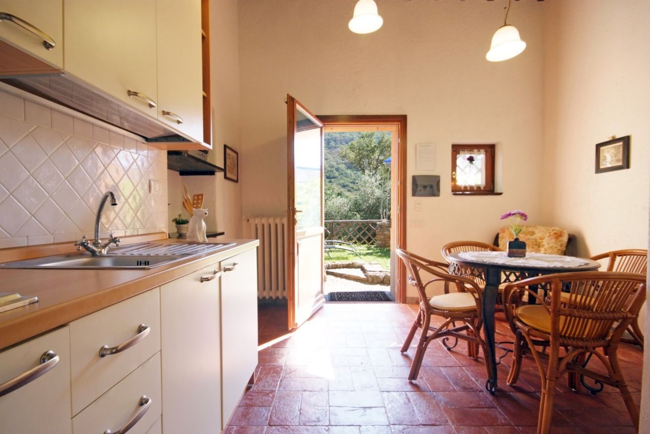 A kitchen with a sink, cabinets, and a dining area with wicker chairs and a table.