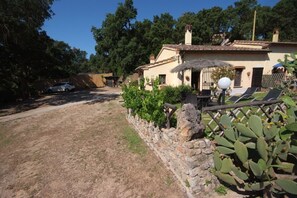Une villa avec un mur en pierre, un cactus et une voiture blanche garée dans l’allée.