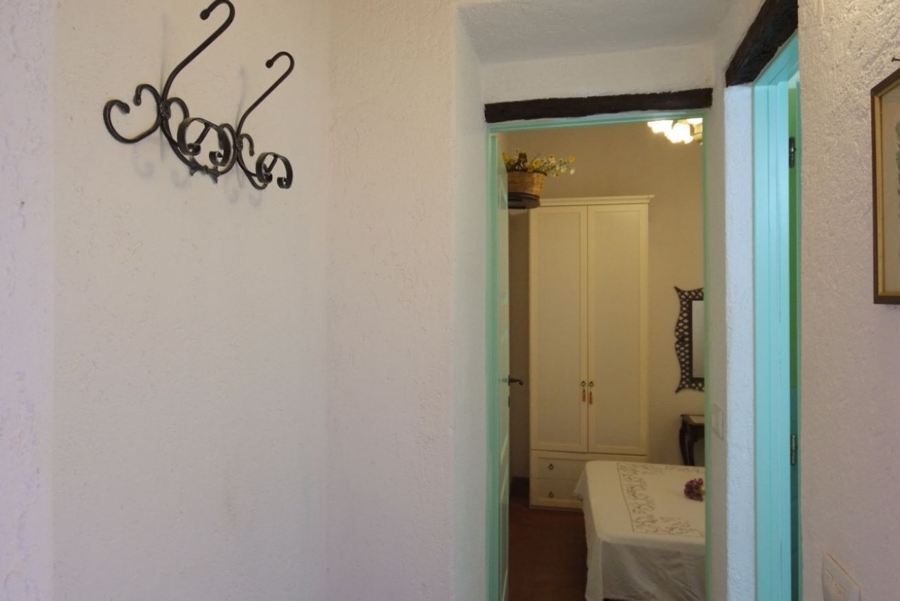 Un pasillo con un detalle decorativo de metal en la pared, una puerta que da a una habitación con cama y un espejo en la pared.