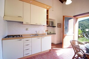 Une cuisine avec des meubles blancs, une cuisinière et un évier. Il y a une petite télévision posée sur une étagère.