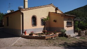A small, single-story building with a tiled roof, a chimney, and a small garden area with potted plants and flowers.