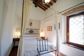 A bedroom with a canopy bed, two bedside tables with lamps, a window with a view, and a decorative ceiling.