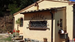 A building with a stone wall, a window with a metal grille, and potted plants. - Villetta Miramare Ortano 1 (Rio)