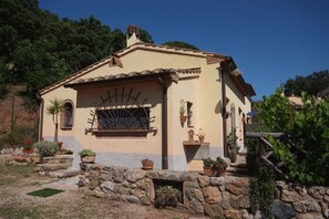Een huis in mediterrane stijl, met een gevel van natuursteen, een pannendak en een kleine tuin met potplanten.