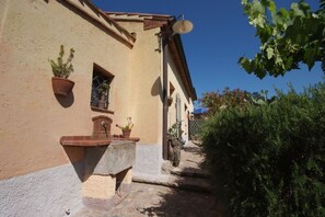 A narrow alleyway with a building featuring a stone bench, potted plants, and a satellite dish.