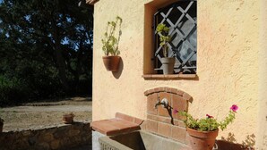 A building with a stone wall, a window with a metal grille, and a brick-built sink with a faucet. - Villetta Miramare Ortano 1 (Rio)