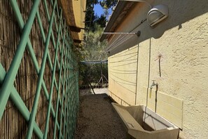 Un espacio exterior reducido con un lavamanos de hormigón, una valla metálica y un portalámparas fijado a la pared.