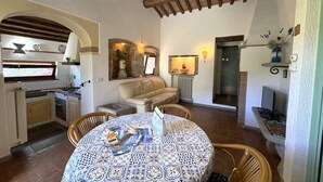 A cozy interior with a kitchen, dining area, and living space, featuring exposed wooden beams, a patterned tablecloth, and a comfortable sofa. - Villetta Miramare Ortano 1 (Rio)