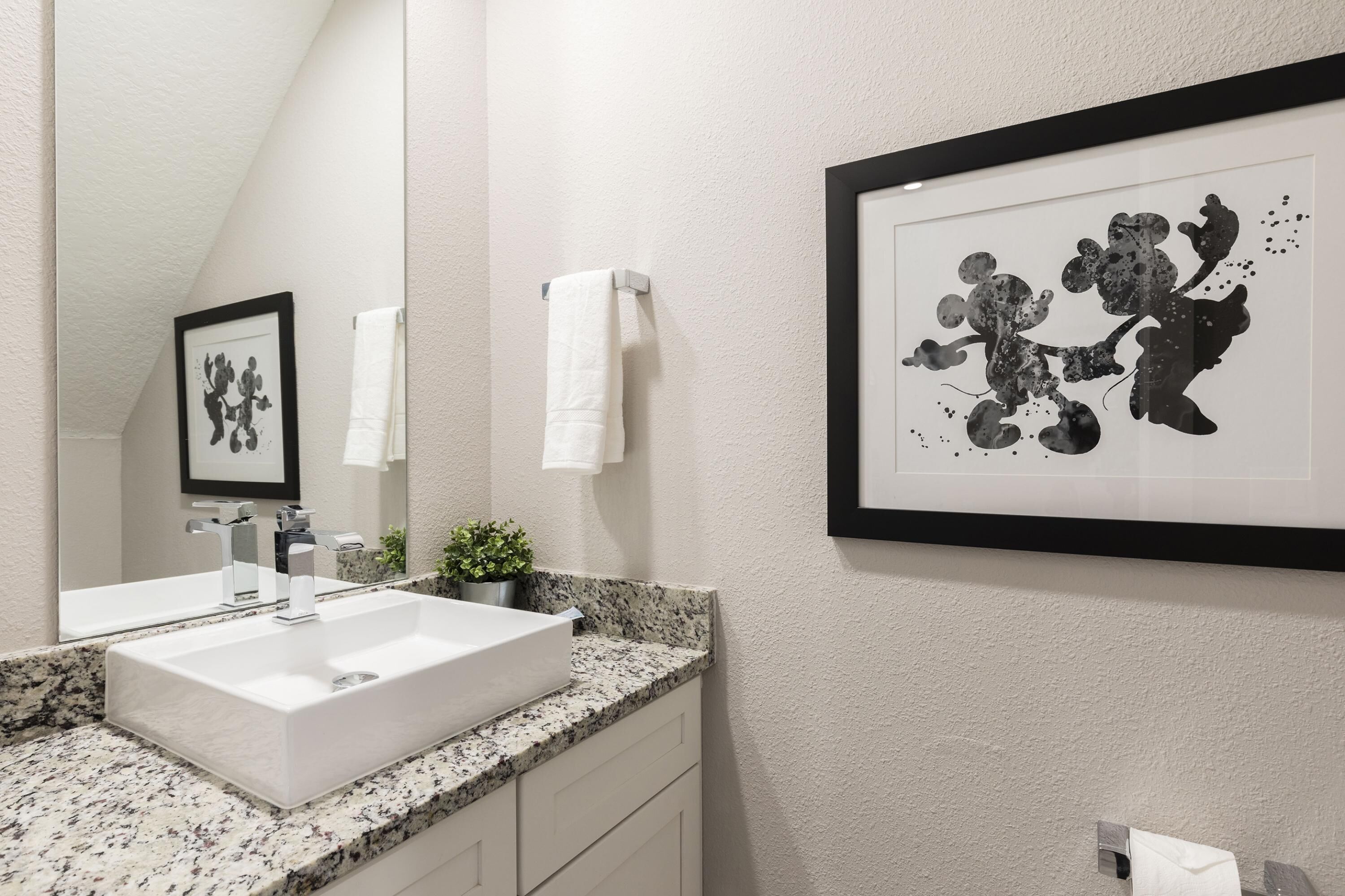 Une salle de bain moderne avec un lavabo blanc, un comptoir en granit et une œuvre d’art abstraite encadrée accrochée au mur.