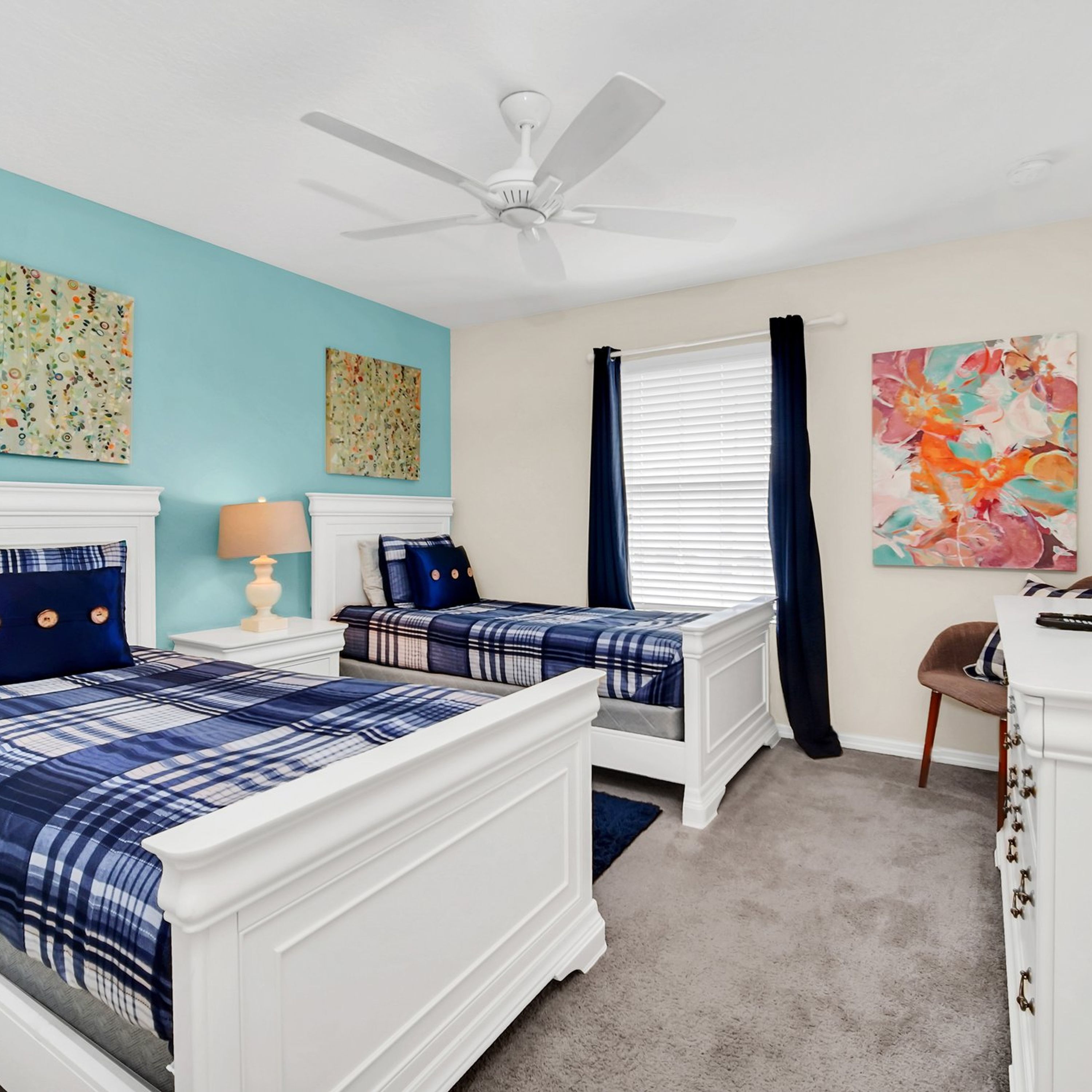 A bedroom with two beds, a ceiling fan, and artwork on the walls.