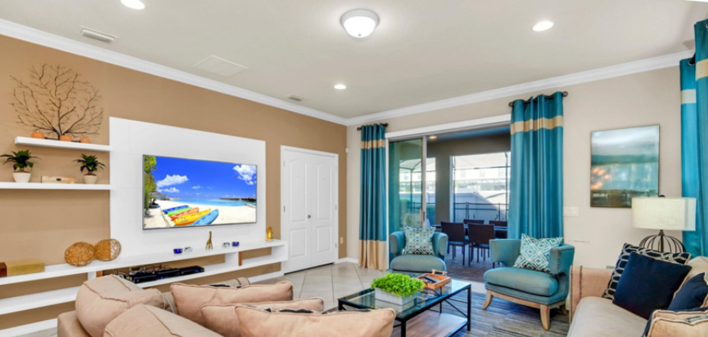 A modern living room with a flat-screen TV, comfortable seating, a glass coffee table, and a view of the outdoors through large windows.