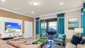 A modern living room with a flat-screen TV, comfortable seating, a glass coffee table, and a view of the outdoors through large windows. - Modern Home Private Pool Sleeps 15 Ww102 (Kissimmee)