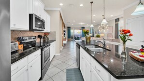 A modern kitchen with white cabinets, a black countertop, stainless steel appliances, and a central island with a sink. - Modern Home Private Pool Sleeps 15 Ww102 (Kissimmee)